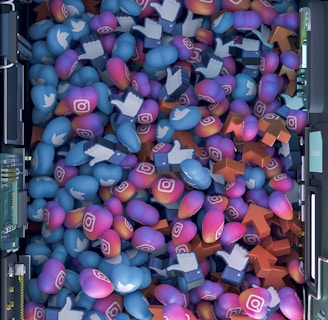 A top-down view of a vibrant pile of colorful icons and symbols representing various social media platforms. Icons include blue Twitter birds, Instagram logos, Facebook-like thumbs up, and orange up arrows. The symbols are situated inside a futuristic, mechanical enclosure, possibly resembling a server or machine.
