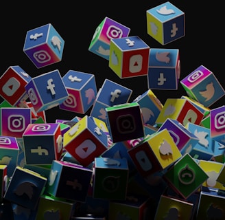 A collection of colorful 3D cubes displaying logos of various social media platforms, including Facebook, Instagram, Twitter, YouTube, and others. The cubes appear to be falling and tumbling over each other against a dark background.